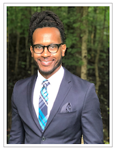 Photo of Jonathan Lucas, Director of Community Programs. He is standing in a gray suit and blue tie and glasses.